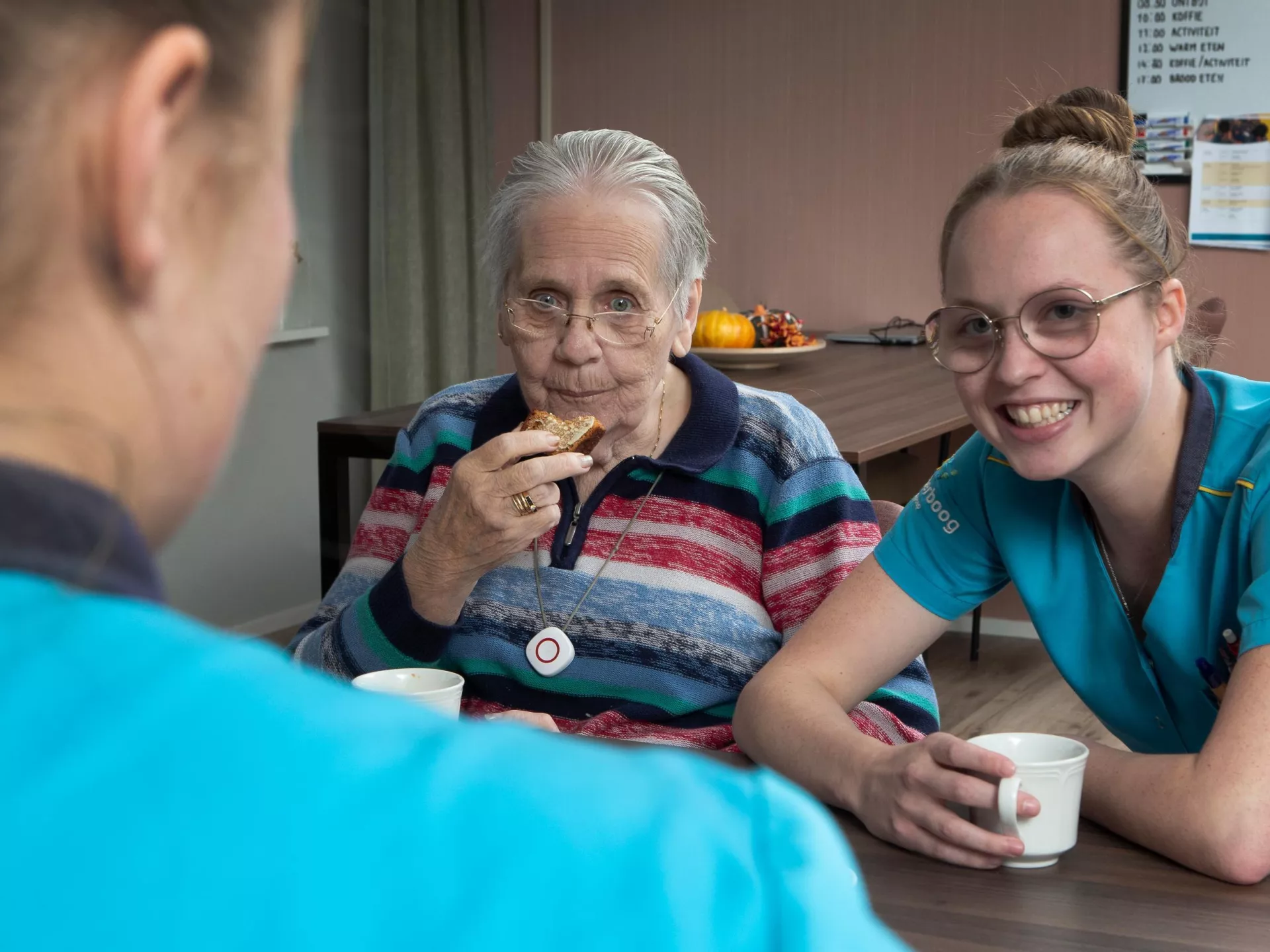 Twee zorgverleners en een oudere vrouw genieten samen van een koffiepauze.